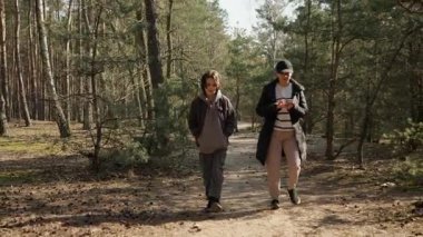 Bir kadın oğluyla ormanda yürürken ve konuşurken akıllı telefonunu kullanır. Modern aile hayatı, çoklu görev ve teknoloji ile kişisel iletişim arasındaki denge..