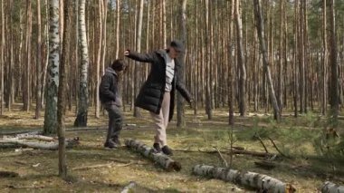 Bir kadın ve çocuğu ormanda oynuyorlar, düşmüş bir kütükte yürüyorlar. Eğlenceli bir aile aktivitesi, denge, koordinasyon ve engelleri birlikte aşma kavramı..