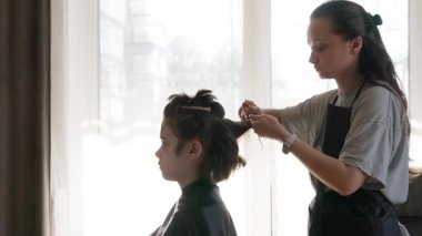 Bir anne kuaför, profesyonel yeteneklerini oğlunun saçını güzel bir şekilde kesmesi için kullanır. Aile içi güven, rahatlık ve ebeveynlerin uzman bakımını gösteren bir sahne..