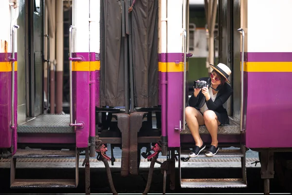 Asyalı kadın elinde kamerayla tren merdiveninde oturuyor.