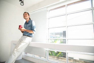 Sabahları elinde kırmızı kahve fincanıyla gülümseyen bir adam.