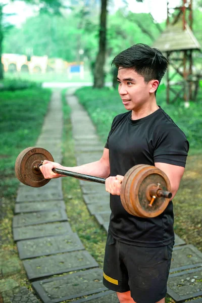 asian guy train his biceps with mini barbell in the park