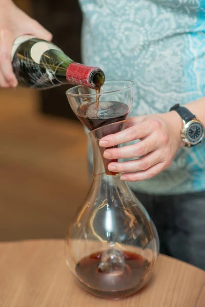 people pouring red wine from bottle to wine decanter