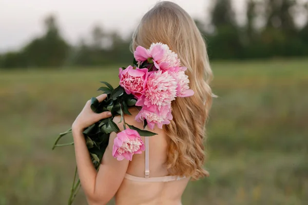 Blonde holds a bouquet of peonies in her hands