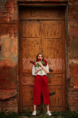 Kırmızı pantolonlu bir kız ve yazın binanın arka planında bir buket kırmızı çiçekle.