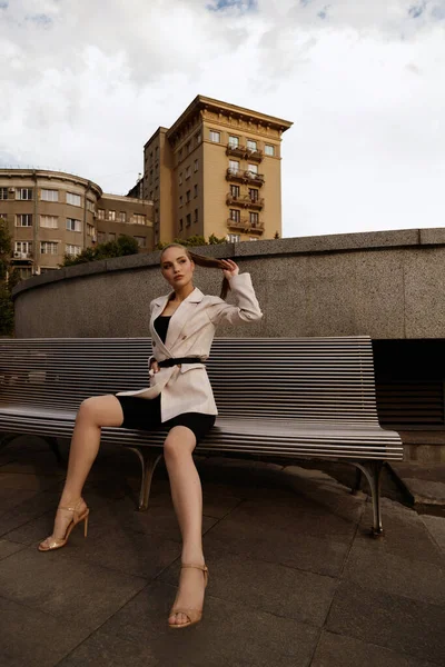 İnce model şehirde motosiklet ve ceketle oturuyor.