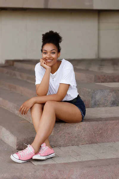 Dark-skinned African-American woman sits on the steps and smiles in the summer