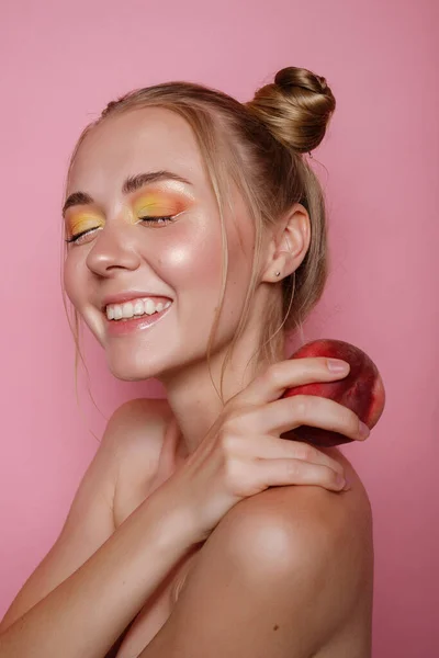 The girl smiles with bright makeup and peach on a pink background. Bright summer photo