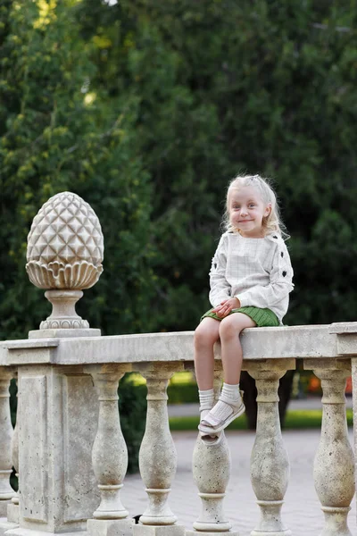 Little girl sits alone in the park and smiles