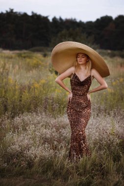 Uzun elbiseli, leopar desenli ve şapkalı ince bir kız.