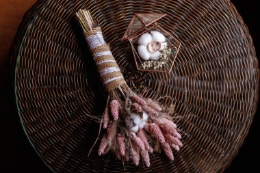 Bir buket kuru çiçek ve cam bir tabutta alyanslar.