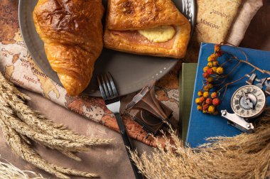 Lezzetli ekmek, kruvasan ve jambon tabakta renkli çiçekler, eski kitaplar ve antik dünya haritasının arka planında antika pirinç anahtarlarla süslenmiş..