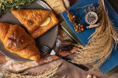 Lezzetli ekmek, kruvasan ve jambon tabakta renkli çiçekler, eski kitaplar ve antik dünya haritasının arka planında antika pirinç anahtarlarla süslenmiş..