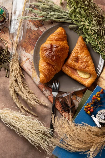 Lezzetli ekmek, kruvasan ve jambon tabakta renkli çiçekler, eski kitaplar ve antik dünya haritasının arka planında antika pirinç anahtarlarla süslenmiş..