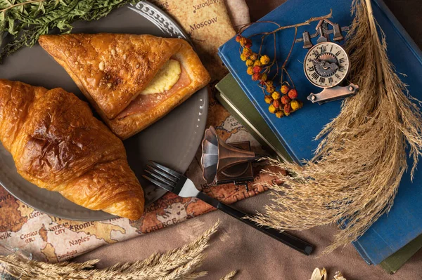 Lezzetli ekmek, kruvasan ve jambon tabakta renkli çiçekler, eski kitaplar ve antik dünya haritasının arka planında antika pirinç anahtarlarla süslenmiş..