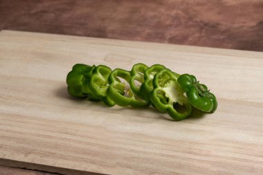 Ahşap kesim tahtasında kahverengi arka planda kesilmiş yeşil biber malzemesi..