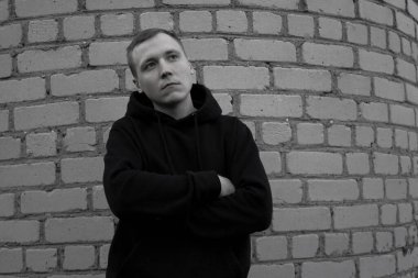 Duvara yaslanmış genç bir adamın siyah beyaz fotoğrafı..