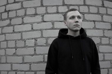 Duvara yaslanmış genç bir adamın siyah beyaz fotoğrafı..