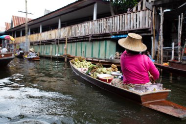 Tayland 'da bir pazarda, uzun kuyruklu bir teknede meyveleri olan bir satıcı kadın. Damnoen Saduak, Tayland