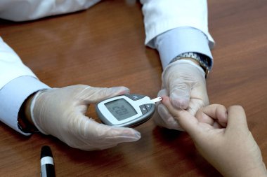 Doktor, hastanın kan şekerini ölçmek için parmak kan testi yapıyor. Glikoz kontrolü
