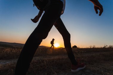 Gün batımında genç bir kızla gezen sırt çantalı genç bir kadının zemin katındaki fotoğrafı. Gerginliğin azaltılması sırasında kırsal alanda yürüyün. Seçici odak.