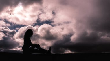 Bulutlu bir gökyüzünde siluet içinde genç bir kız