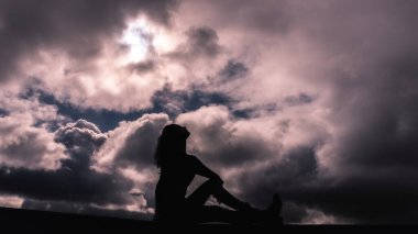 Bulutlu bir gökyüzünde siluet içinde genç bir kız