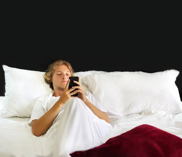 young man using smartphone in bed at home