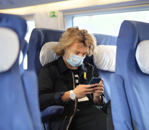 Young  man wearing  surgical face mask waiting for the train,using smartphone, typing a message on the phone.