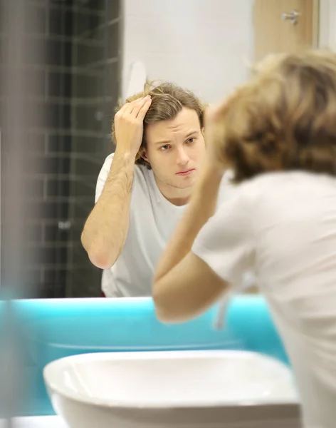 young man looking in the mirror,combing his hair,looking at problems on face