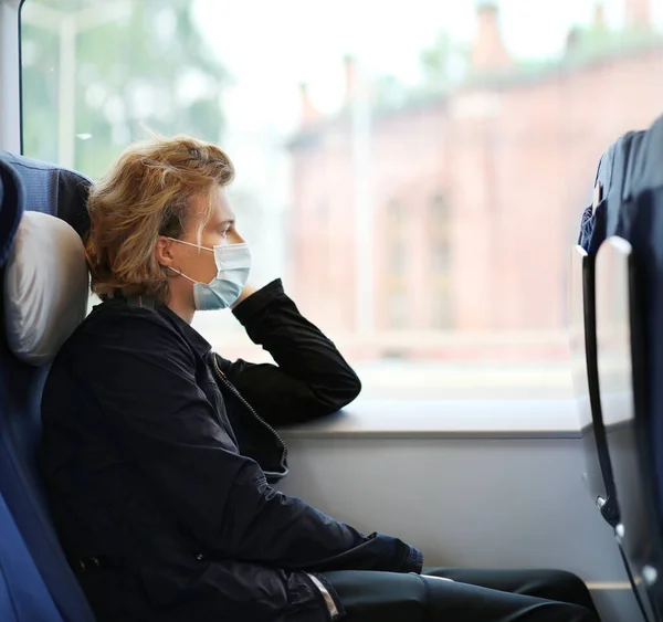 Young  man wearing  surgical face mask waiting for the train,using smartphone, typing a message on the phone.