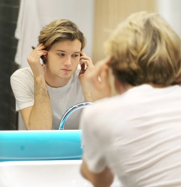 young man looking in the mirror,combing his hair,looking at problems on face