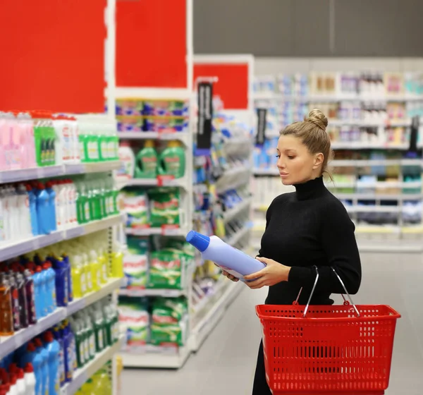 Woman shopping in supermarket reading product information.(washing powder,detergent,shampoo, soap)