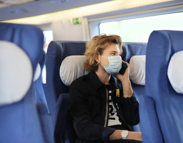 Young  man wearing  surgical face mask waiting for the train,using smartphone, typing a message on the phone.