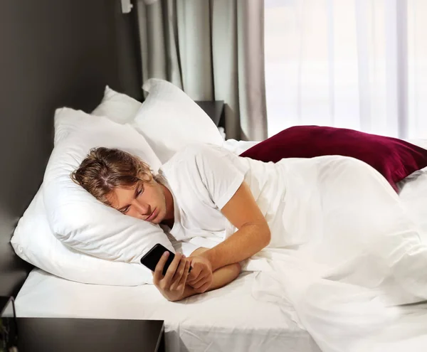 young man using smartphone in bed at home
