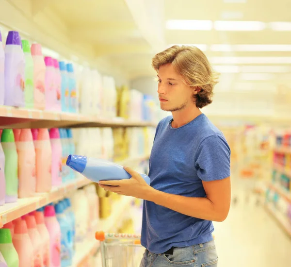 man shopping in supermarket reading product information(washing powder, soap, shampoo, pampers,toilet paper)