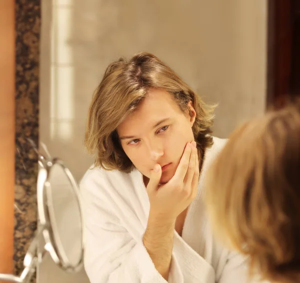 young man looking in the mirror,combing his hair,looking at problems on face