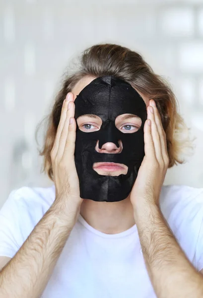 Anti-aging eye therapy.  young man taking care of his undereye wrinkles applying facial mask. man  moisturizing face mask. Cosmetology and skin care concept.