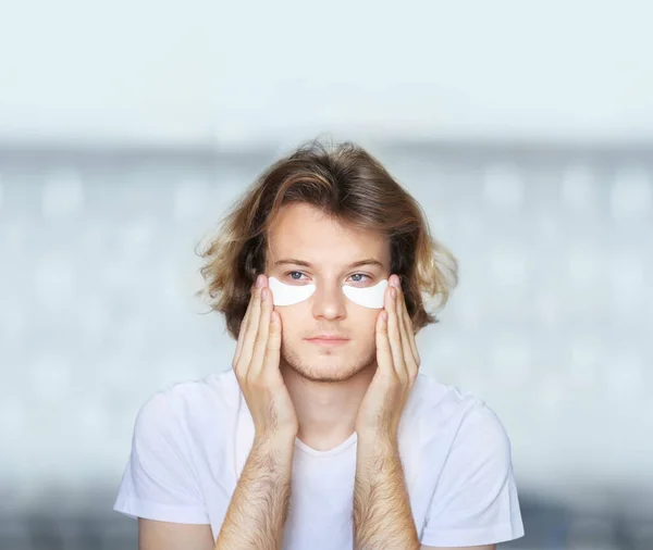 Anti-aging eye therapy. young man taking care of his undereye wrinkles applying facial mask. Cosmetology and skin care concept.Dark Circles.Eye patches.