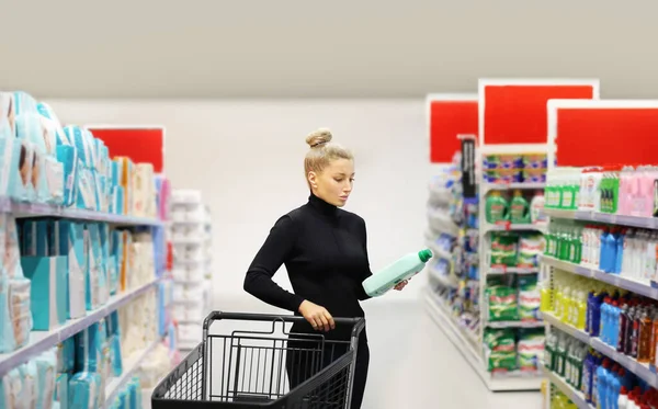 Woman shopping in supermarket reading product information.(shampoo, soap, shower gel,)