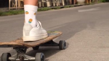 Güzel, beyaz dövmeli, kot şortlu, ekose gömlekli, gün batımında ağır çekimde yürüyen kaykaylı bir kadın.  