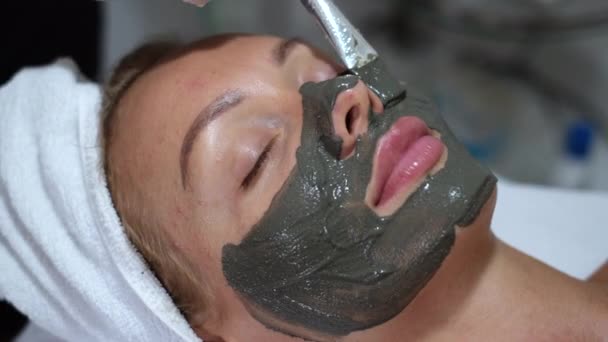 Kosmetikerin tragen Tonmaske mit Pinsel auf junge hübsche Frau Gesicht in Schönheitsklinik, Wellness-Salon. Kosmetikerin macht Schönheit Gesichtspflege Verfahren zu kaukasischen europäischen weiblichen    