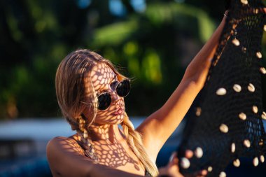 Örgü pelerininden bir gölge düşer. Genç Avrupalı, siyah modaya uygun, parlak bikinili, tropik yüzme havuzu, yaz havası, yaz havası.... 