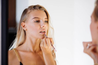 Doğal makyajlı genç ve güzel bir kadın aynaya bakıyor ve renkli dudakları kaleme alıyor. Yumuşak, pürüzsüz ten.  