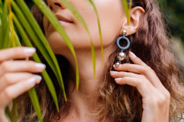 Bronzlaşmış Avrupalı bir kadının açık hava portresi. Kısa saçlı, yuvarlak, palmiye yapraklı, tropikal arka planı olan bir kadın..