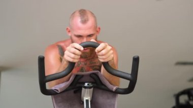 Avrupalı yakışıklı, kaslı, güçlü, sakallı, spor salonunda kardiyo bisikleti süren, hızlı binen, güçlü bir adam. Spor salonunda hızlı bisiklet sürme    