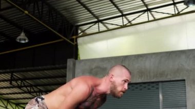 Yakışıklı, dövmeli, spor kıyafetli, sakallı, spor salonundaki çaydanlık çanlarıyla çalışan genç adamın yan görüntüsü.    