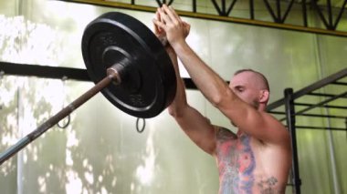 Spor salonunda sakallı, güçlü bir adam dövmesi var. Halter egzersizi yapan kaslı vücutçu. Genç sporcu halter yarışmalarına katılıyor..      