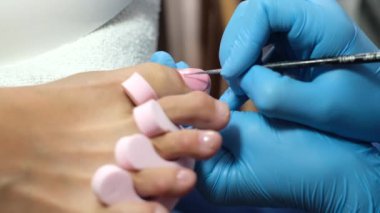 Ev kuaförü pedikür. Ayak bakımı ve çivi. Profesyonel pedikür süreci işte. Mavi eldivenli usta açık pembe jel cilası sür..    