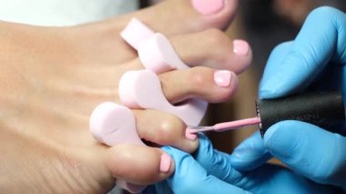 Ev kuaförü pedikür. Ayak bakımı ve çivi. Profesyonel pedikür süreci işte. Mavi eldivenli usta açık pembe jel cilası sür..    